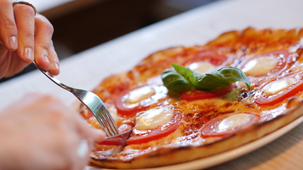 a person cutting into a margherita pizza